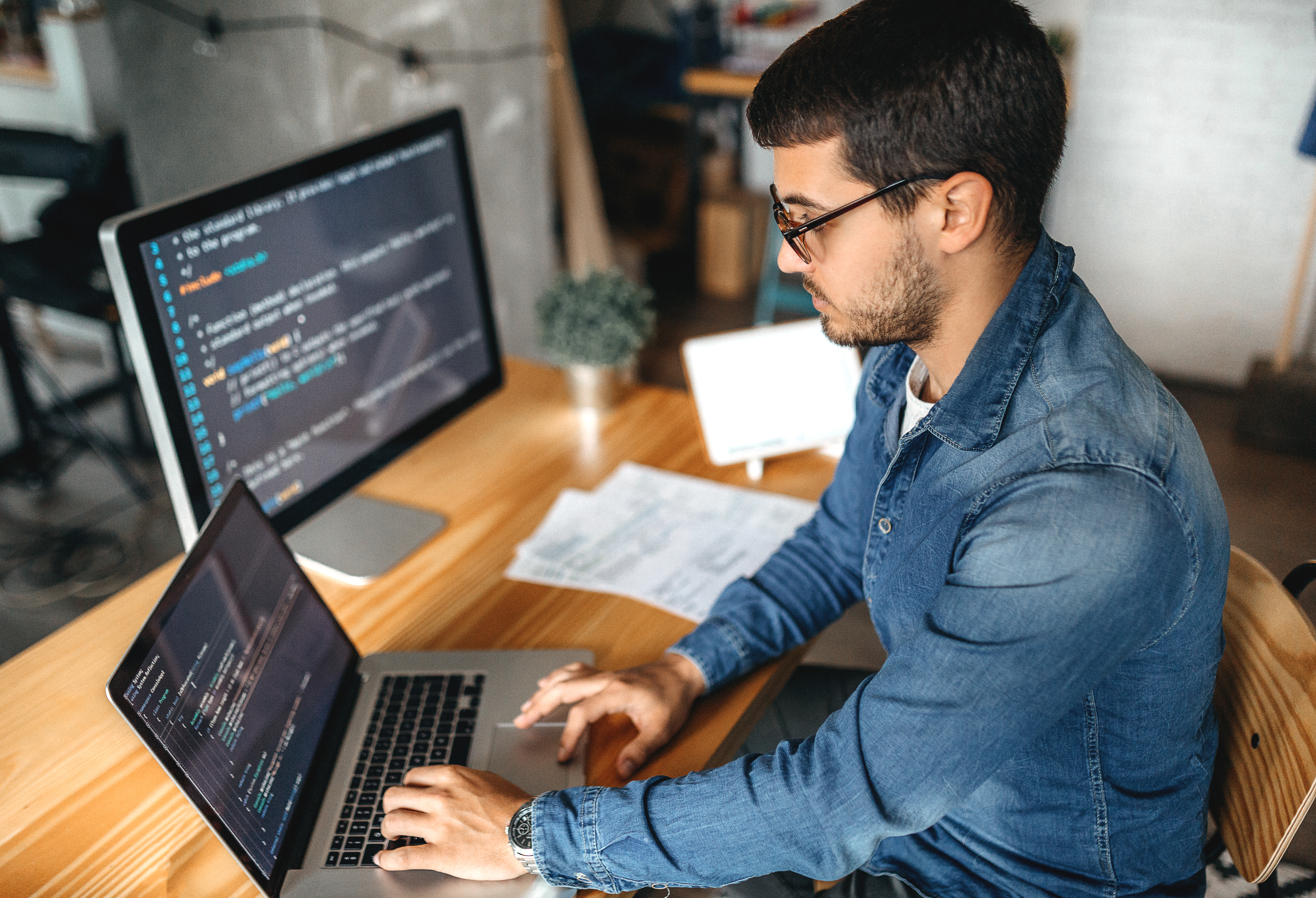 Man typing on laptop at desk with monitor