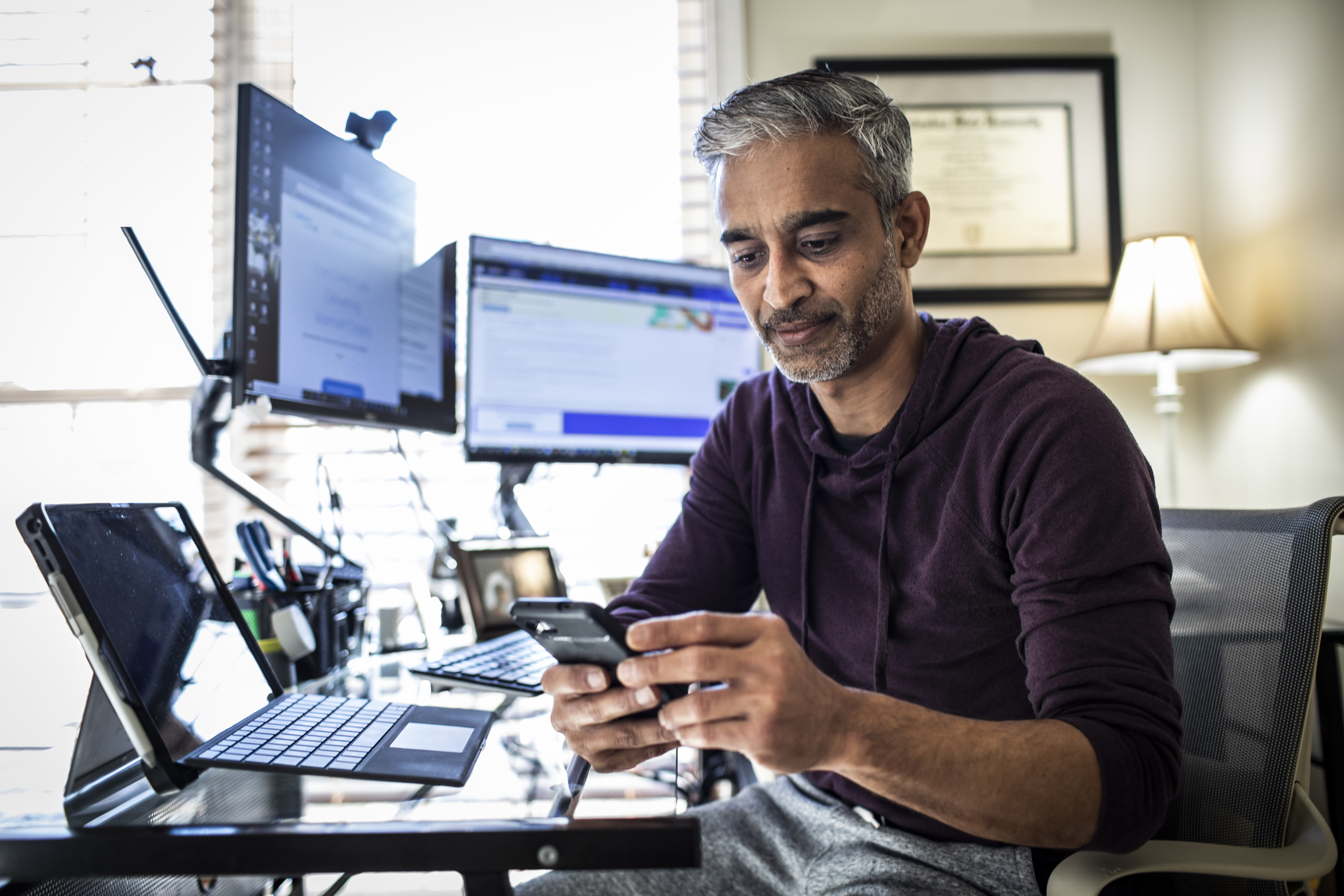 Man looking at phone at desk with computers