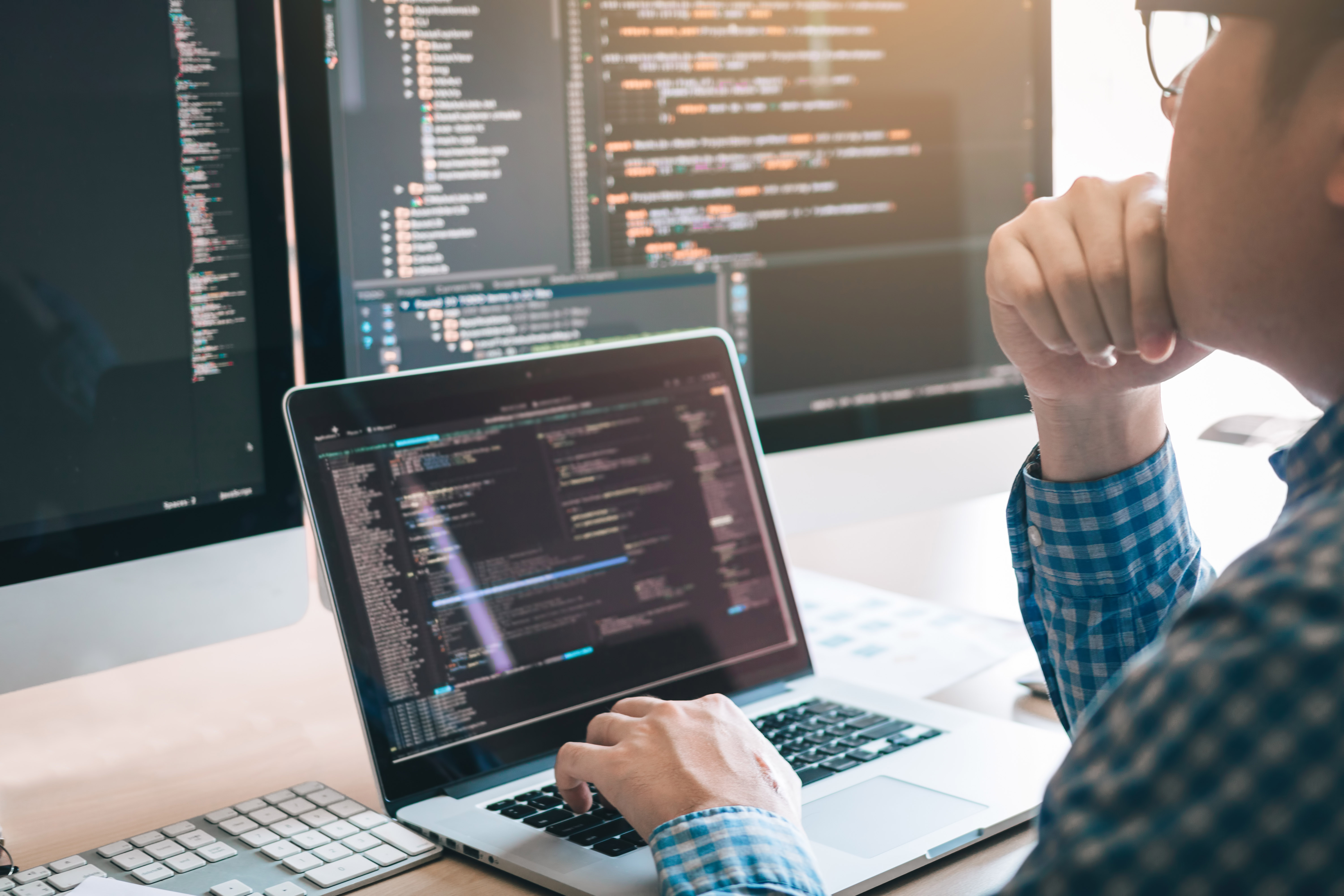 Man looking at laptop and computer screens with software code
