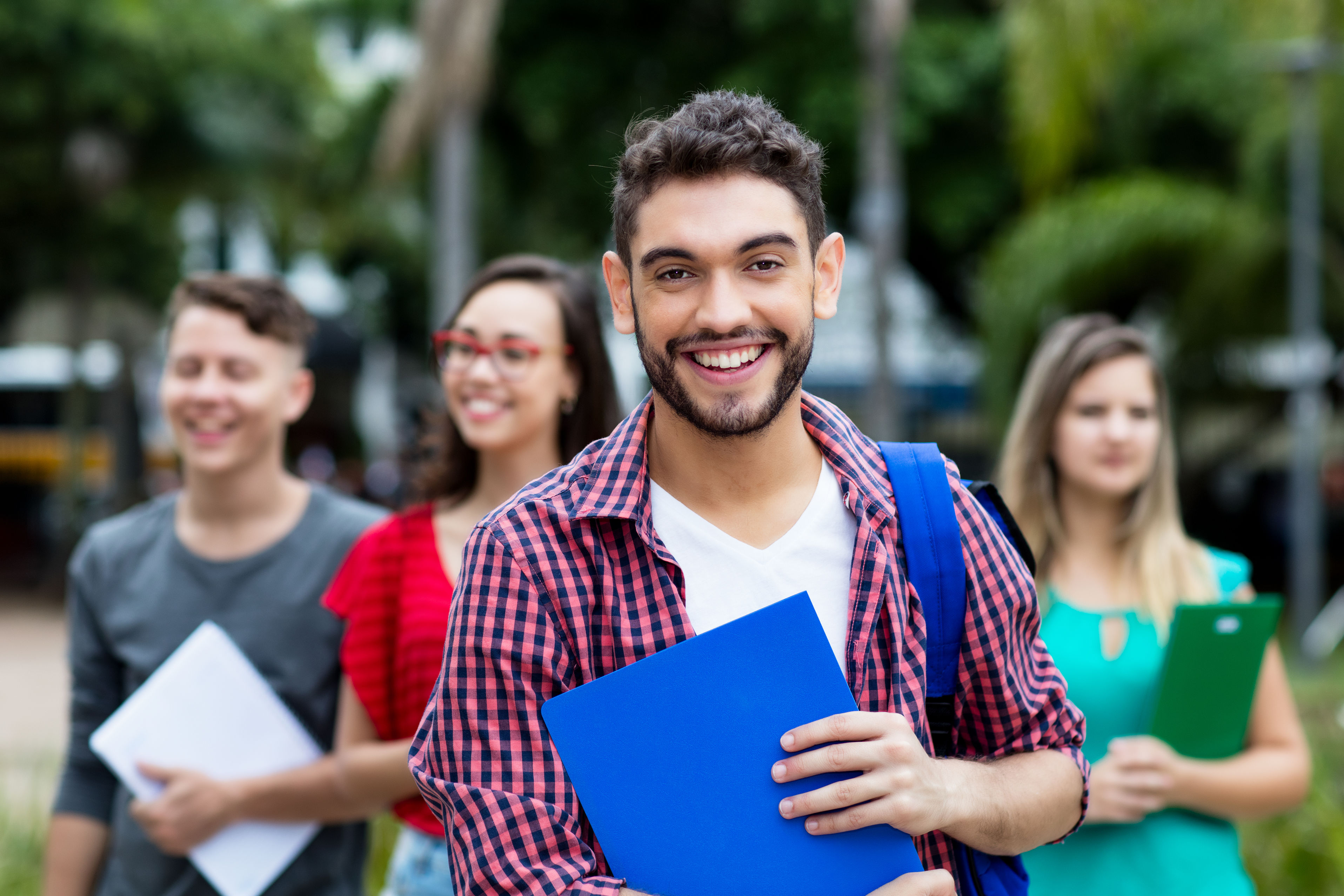 Four students walking and smiling carrying folders or clipboards
