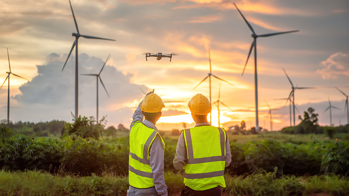 Picture of two men standing in a wind farm with a drone at sunset