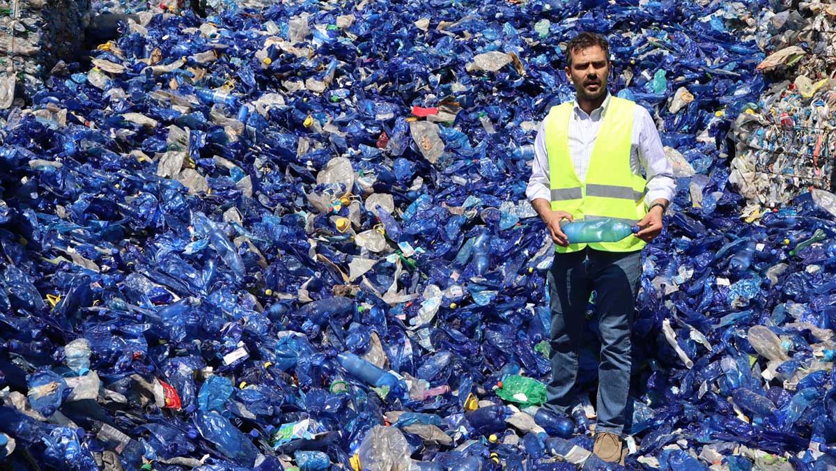 Keep Sea Blue founder Lefteris Bastakis stands in front of a pile of recovered plastic bottles