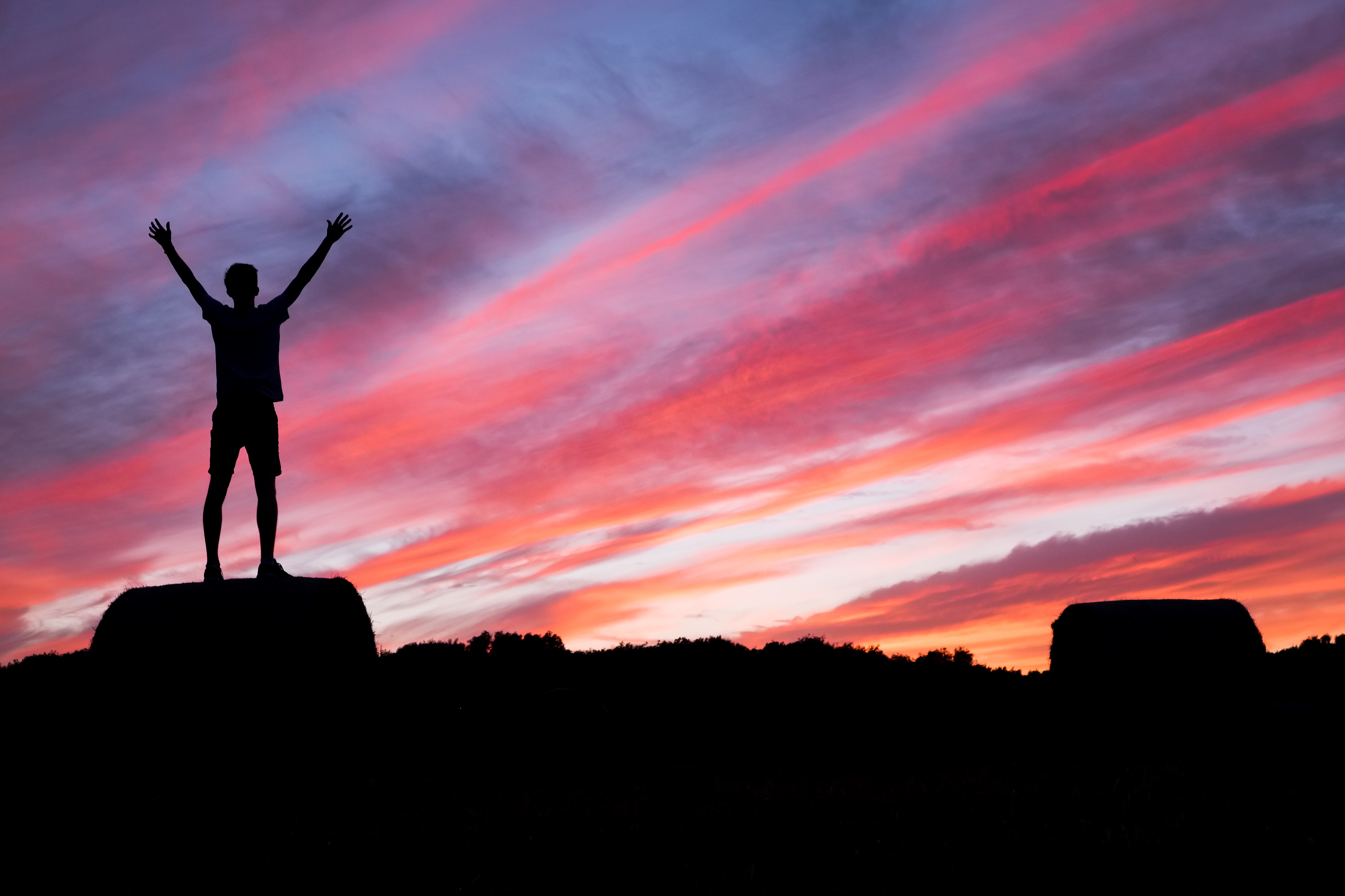Person with arms raised in silhouette against sunset