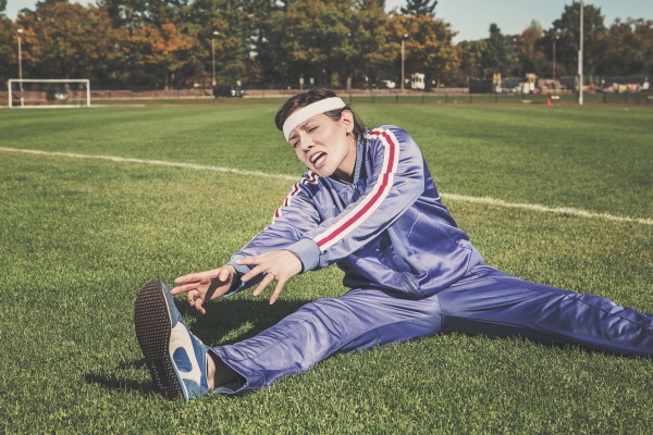 Woman in tracksuit stretching to touch her toes while sitting