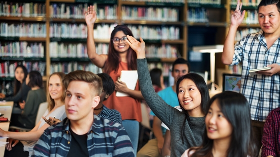 A photograph that shows students in a library, smiling and raising their hands.